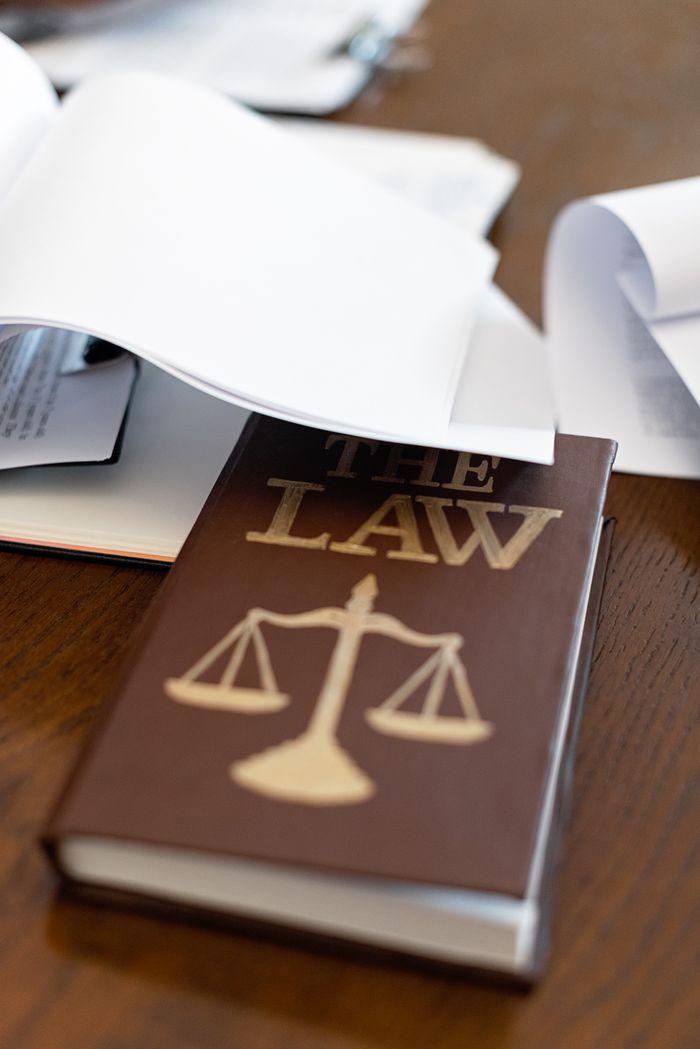 team-04 Close-up of a law book with scales icon on a wooden desk covered in papers.