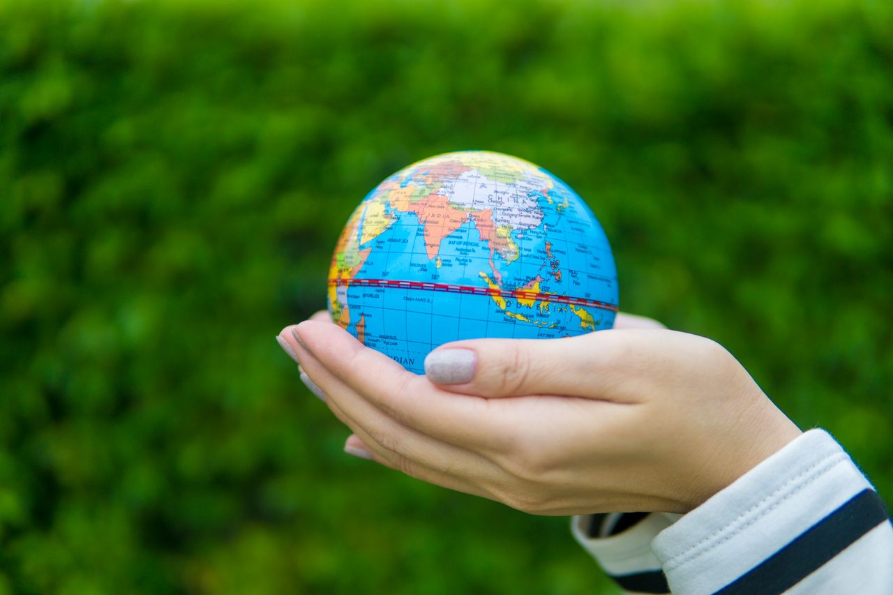 services-02 Close-up of hands gently cradling a miniature globe against a green backdrop.